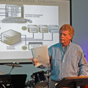 Keith Bennett standing at a lectern teaching a class, a projected slide behind him reading Relational Data Base Theory.